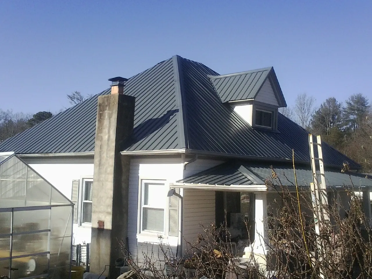 Dark blue standing seam metal roof on a white farmhouse with dormer — Slate & Tile Roof Repair by Roofing Brothers in Bushnell