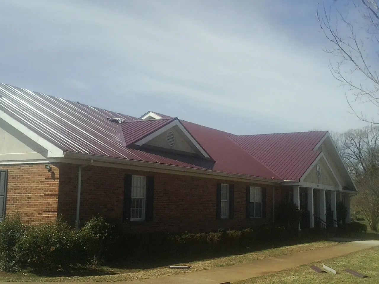 Red metal roof with gabled entries on a long brick building, from a Hail Damage Roof Repair job in Bushnell