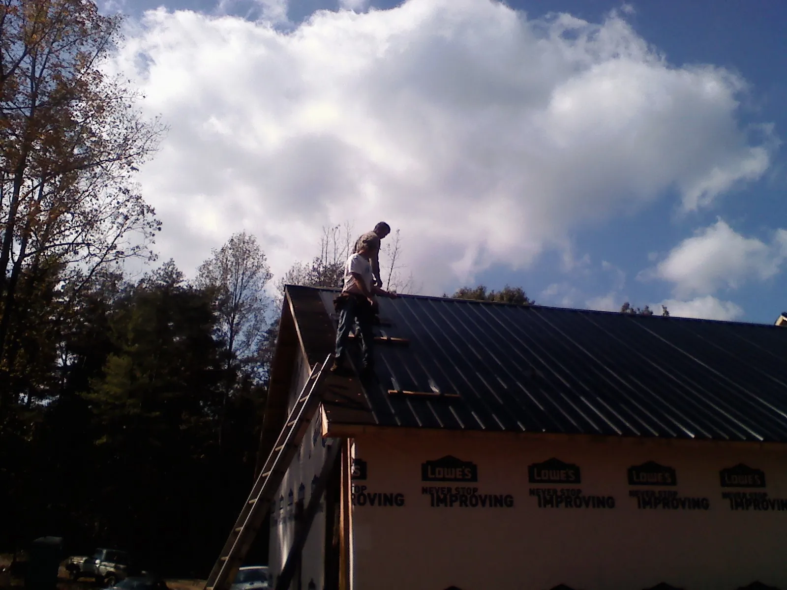 Roofer fastening dark metal panels high against a cloudy sky, from a Roof Inspection job in Bushnell
